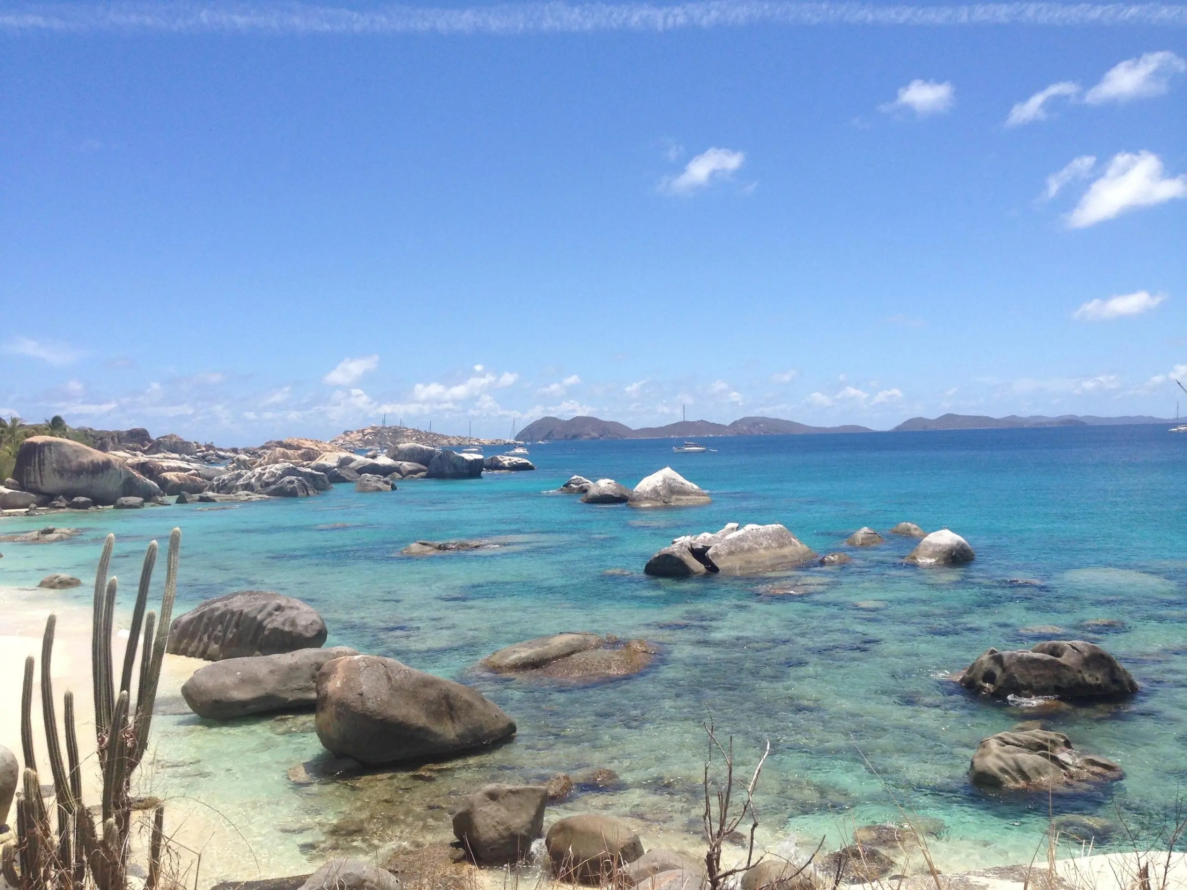 Rocky beach with clear blue water and distant islands under a clear sky.