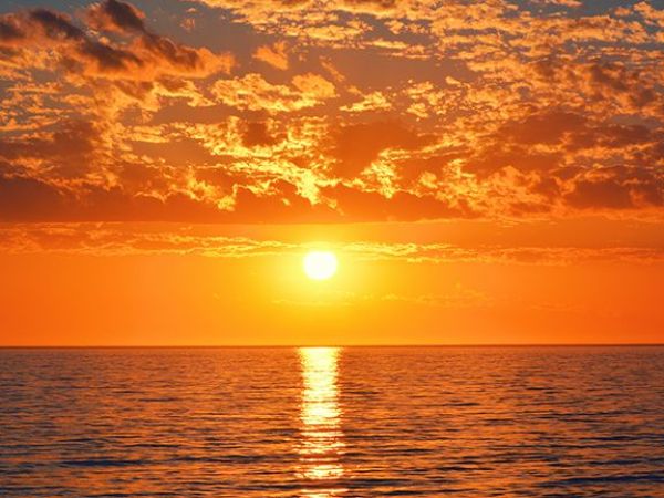 Vibrant sunset over ocean with orange sky and clouds.