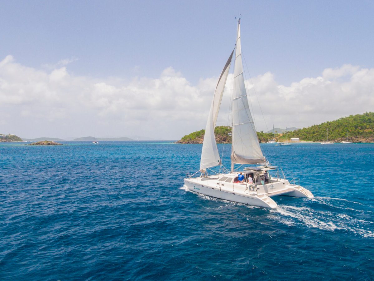 Catamaran sailing on blue ocean with distant islands and cloudy sky.