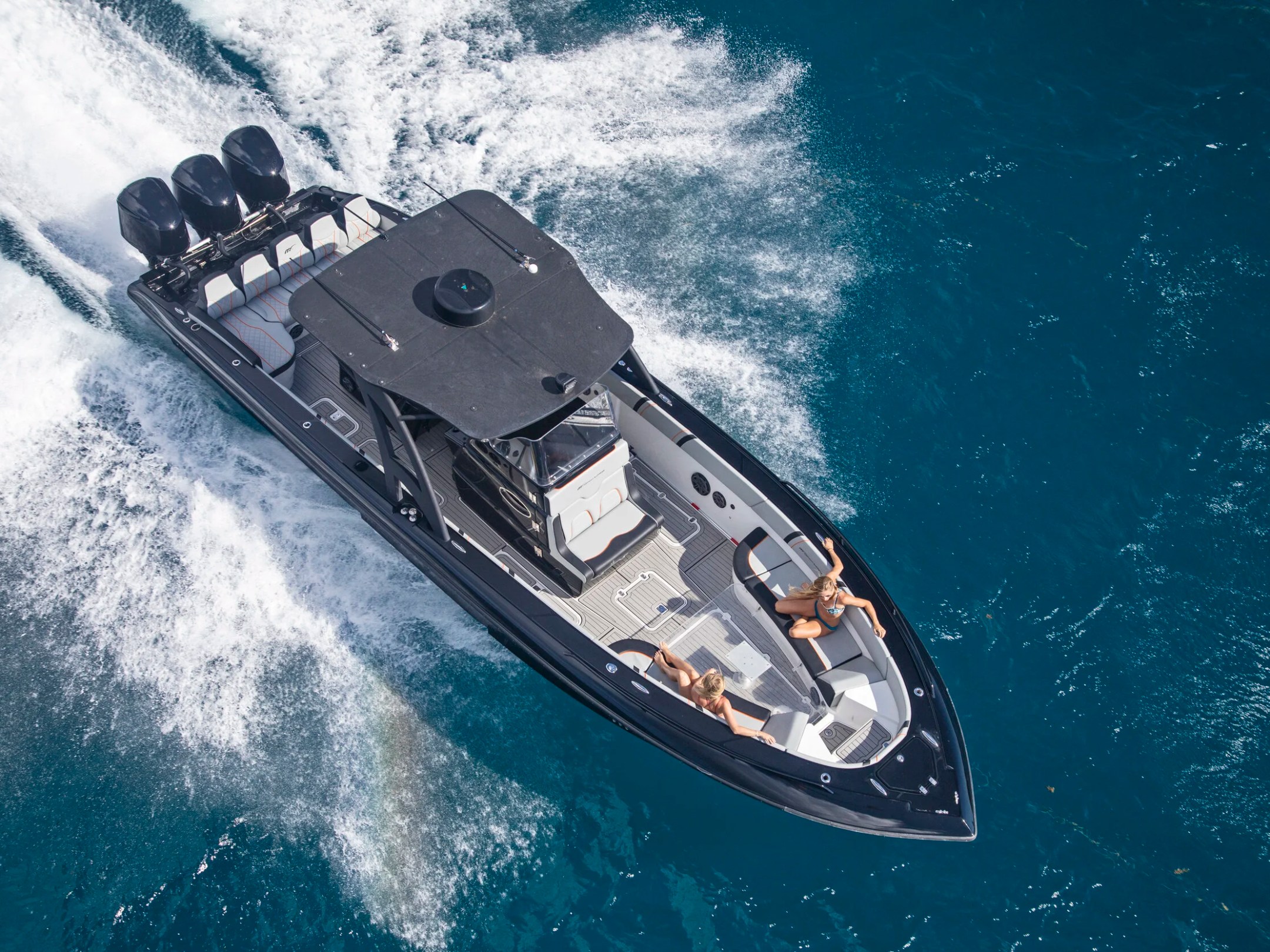 Aerial view of a black speedboat with four engines moving swiftly on blue water.