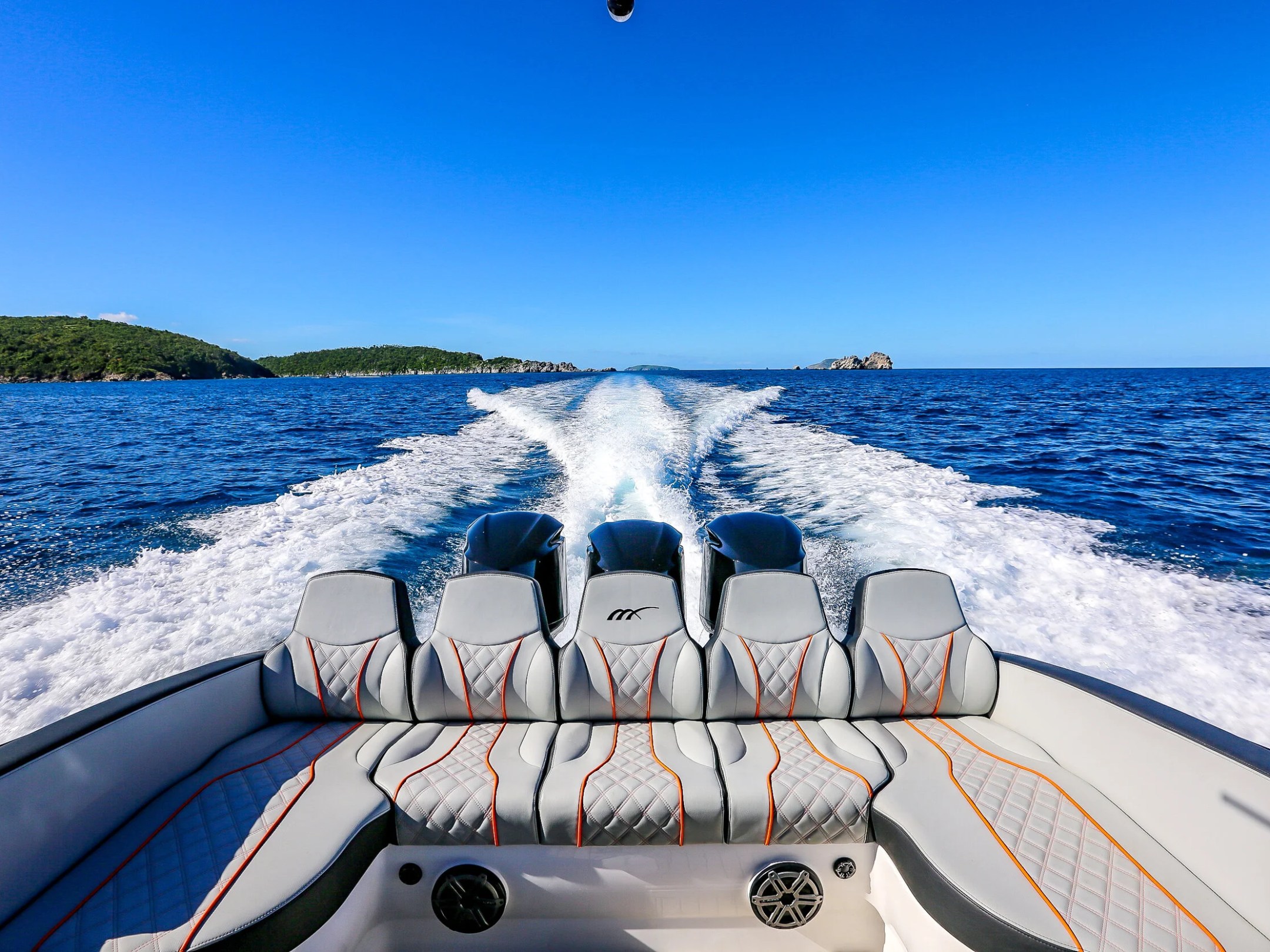 View from speedboat's rear with wake trails on blue ocean under clear sky.
